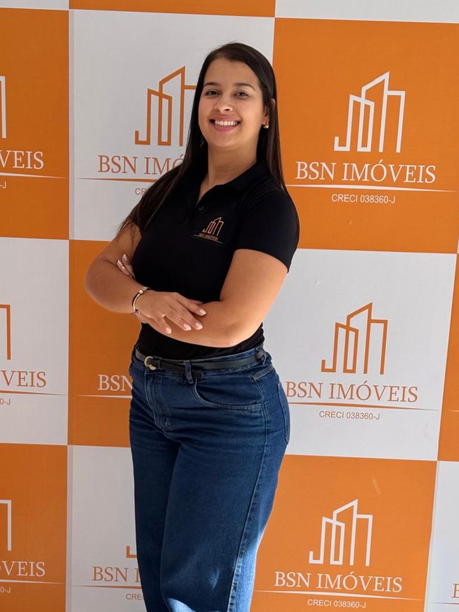 Corretora da BSN Imoveis no escritorio, diante do painel da marca com CRECI 038360-J